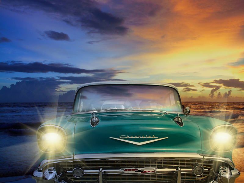 classic car on the beach with headlights on at sunset