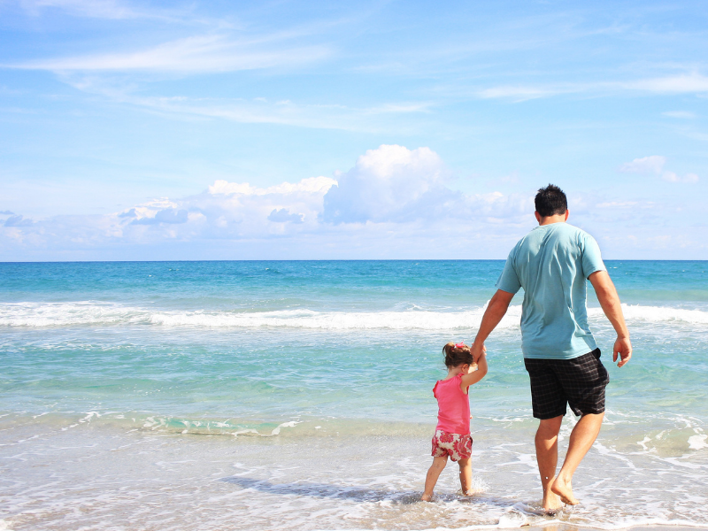 man walking on the beach holding the hand of a small girl